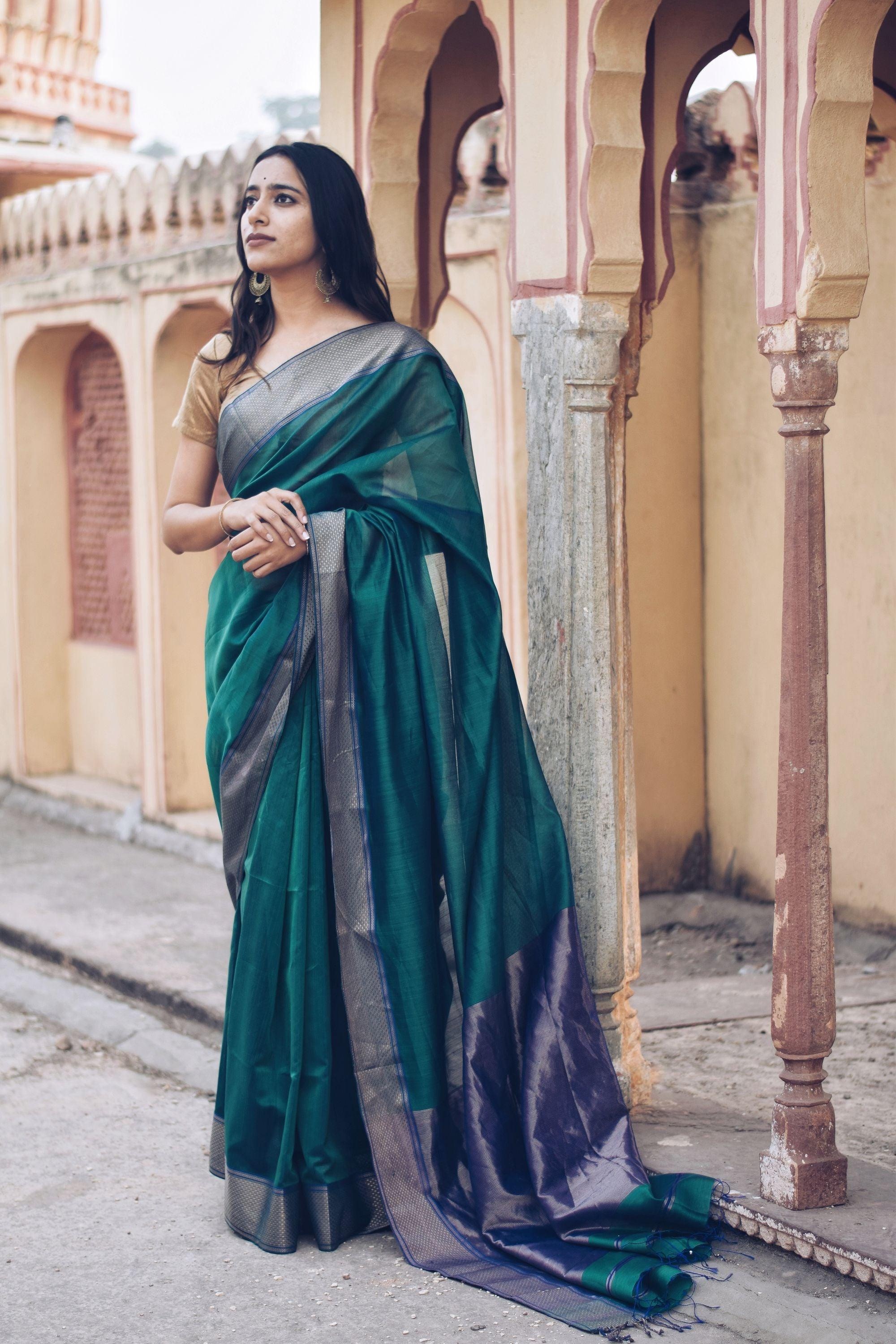 Woman in a teal Maheshwari silk-cotton saree standing amid heritage architecture