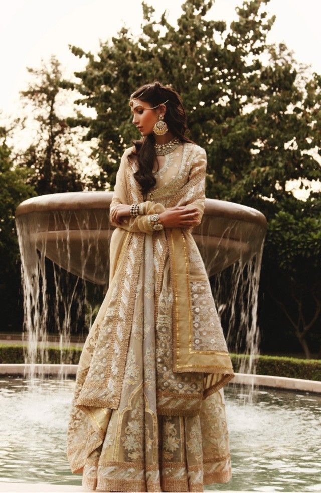 Woman in an ivory embellished anarkali gown beside a fountain